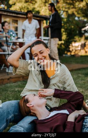 Glückliche Frau, die auf dem Schoß einer Freundin liegt, die auf Gras im Garten sitzt Stockfoto