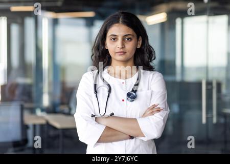 Selbstbewusste Ärztin mit Stethoskop um den Hals gekreuzte Arme in der modernen Praxis. Professioneller Ausdruck, medizinisches Umfeld. Steht für Gesundheitswesen, Vertrauen und Engagement. Stockfoto