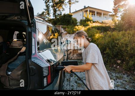 Junge, der den Ladestecker einsteckt, während er in der Nähe eines Elektroautos steht Stockfoto