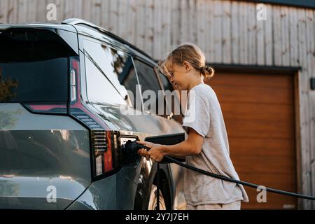 Seitenansicht des Jungen, der den Ladestecker im Elektroauto auf der Einfahrt einsetzt Stockfoto