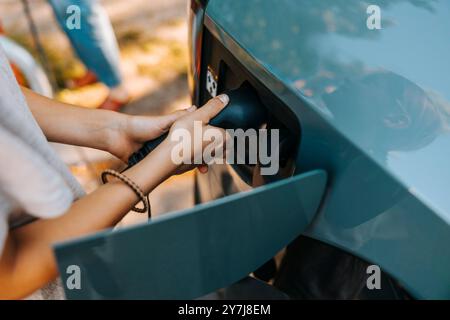 Hochwinkelansicht des Jungen, der den Stecker beim Laden des Elektroautos einsteckt Stockfoto