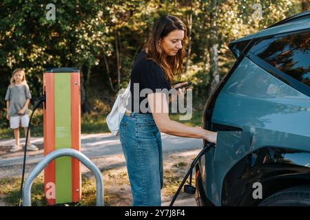 Seitenansicht der Frau, die den Elektrostecker nach dem Aufladen des Autos an der Station entfernt Stockfoto