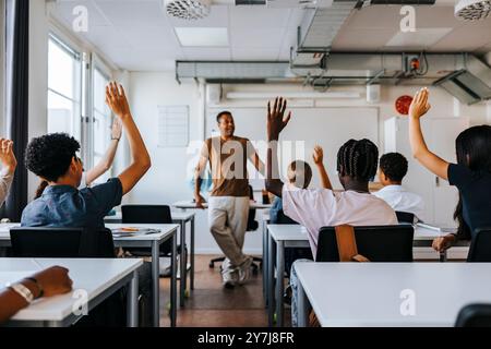Rückansicht männlicher und weiblicher Mittelschüler mit erhobener Hand während des Lehrerunterrichts in der Schule Stockfoto