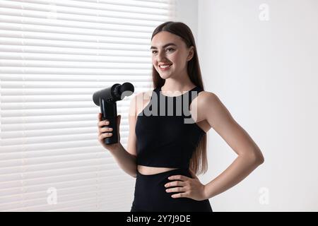 Junge Frau mit perkussiver Massagepistole drinnen Stockfoto