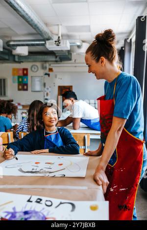 Lächelnde Kunstprofessorin, die männlichen Schüler während des Kunstunterrichts in der Schule unterstützt Stockfoto