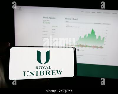 Person, die ein Mobiltelefon mit dem Logo der dänischen Brauerei Royal Unibrew auf dem Bildschirm vor der Business-Webseite hält. Schwerpunkt auf dem Display des Telefons. Stockfoto