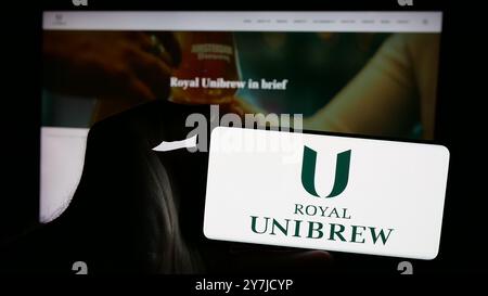 Person, die ein Mobiltelefon mit dem Logo der dänischen Brauerei Royal Unibrew auf dem Bildschirm vor der Website des Unternehmens hält. Schwerpunkt auf dem Display des Telefons. Stockfoto