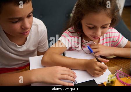 Zwei Kinder lernten, schrieben in Notizbüchern an einem Holzschreibtisch und förderten das Lernen und die Zusammenarbeit in der häuslichen Umgebung. Stockfoto