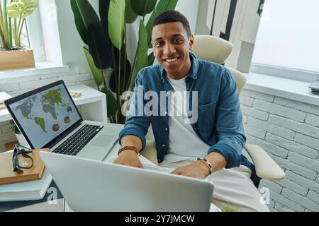Draufsicht auf einen glücklichen Mann mit gemischtem Rassen, der im Büro mit einem Laptop arbeitet Stockfoto