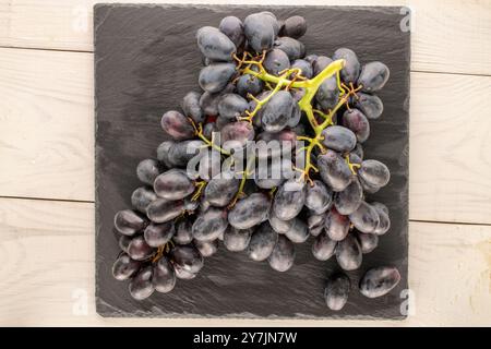 Ein Haufen reifer schwarzer Trauben mit Schieferstein auf Holztisch, Makro, Blick von oben. Stockfoto