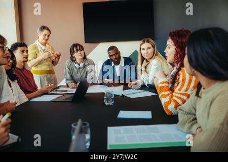 Verschiedene Gruppen von Klassenkameraden nehmen aktiv an einer Lerndiskussion an einem Tisch Teil, um die Zusammenarbeit und Bildung in einem modernen Klassenzimmer zu fördern Stockfoto