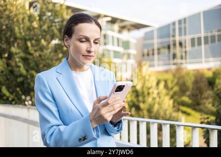 Geschäftsfrau steht draußen vor einem modernen, nachhaltigen Bürogebäude und blickt auf ihr Smartphone Stockfoto