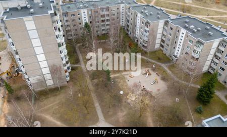 Blick aus der Vogelperspektive auf einen Wohnkomplex mit mehreren Apartmentgebäuden, die einen kleinen Spielplatz umgeben. Die Gegend ist mit Bäumen und Pfaden angelegt Stockfoto