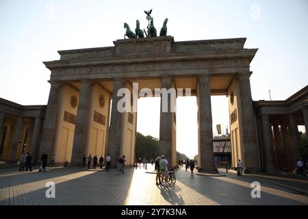 Touristen, zwei von ihnen auf Fahrrädern vor dem Brandenburger Tor mit einer Bronzeskulptur einer Quadriga auf der Spitze, berühmtes Wahrzeichen, hinter der Sonne beleuchtet Stockfoto