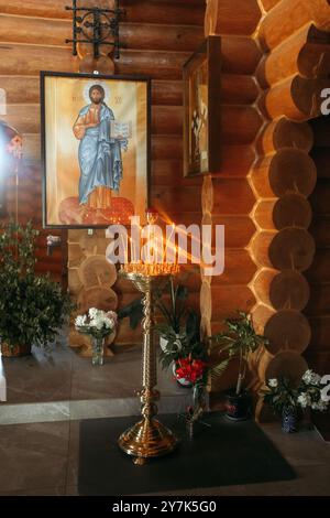 Ein goldener Kandelaber mit brennenden Kerzen steht in einer Holzkirche, in Sonnenlicht getaucht. Das Licht wirft ein warmes Licht auf die umliegenden Wände und einen nea Stockfoto