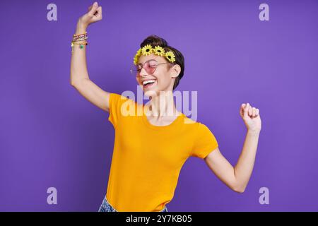 Fröhliche junge Frau mit floralem Kopfkranz, während sie vor violettem Hintergrund steht Stockfoto