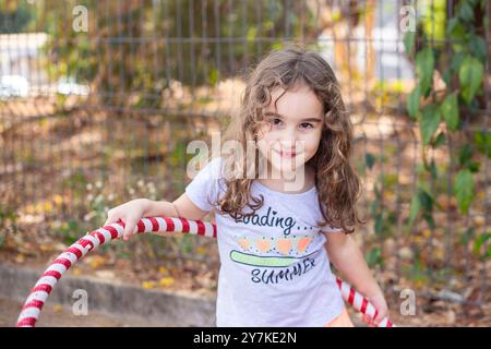 Goiania, Goias, Brasilien – Setembro 20, 2024: Ein Kind, das mit einem rot-weiß gestreiften Hula-Hoop im Freien spielt. Stockfoto