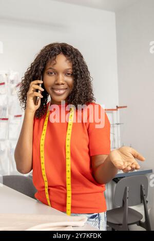 Schneiderin in orangefarbenem T-Shirt, der am Telefon spricht, während er Stoff schneidet Stockfoto