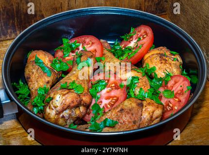 Gebratene Hähnchenschenkel mit Tomaten und Petersilie auf Holzoberfläche. Stockfoto