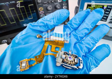 Flex-Leiterplatte, Sensor oder Linse des CD-DVD-Laufwerks Aufnahmekopf. Elektronische Bauteile und Flachbandkabel auf der fachkundigen Hand im Technischen Labor. Stockfoto