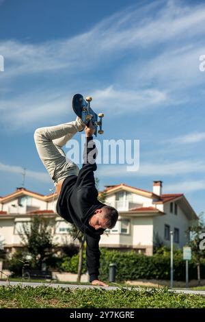 Vertikaler Skater, der ein beeindruckendes Flugmanöver durchführt, ihr Skateboard hochhebt und gleichzeitig kopfüber auf dem Rand der Skatepark-Schale balanciert Stockfoto