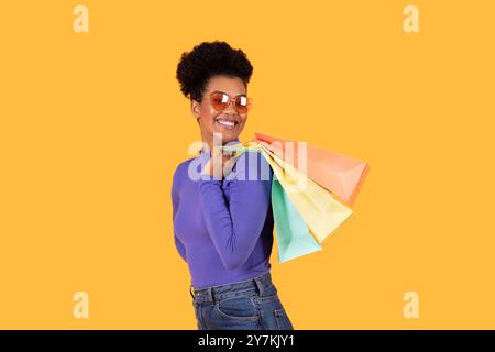 Eine fröhliche junge Frau mit lockigem Haar lächelt und trägt eine Sonnenbrille Stockfoto