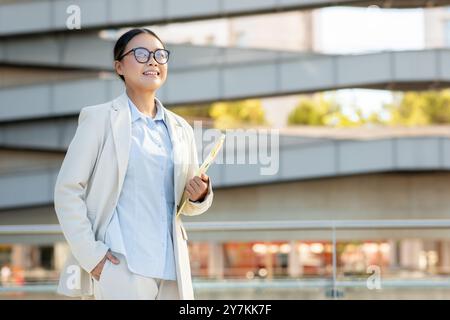 Professionelle Frau in einem leichten Anzug lächelt selbstbewusst in einer urbanen Umgebung Stockfoto