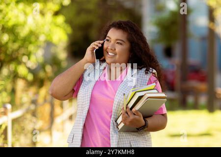 Schüler telefoniert am Telefon, während er Bücher an einem sonnigen Tag im Freien trägt Stockfoto