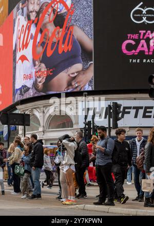 London, England, April 30 2023: Menschen im Piccadilly Circus warten darauf, die Straße an einem geschäftigen Tag mit den großen Bildschirmen dahinter zu überqueren Stockfoto