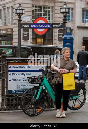 London, England, April 30 2023: London, England, April 30 2023: Frau stehend im Piccadilly Circus, mit einer selfridges-Tasche, neben einem Fahrrad am Under Stockfoto