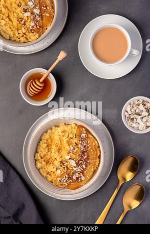 Lebensmittelfotografie von Hirsebrei mit karamelisierter Banane, Pekannuss, Nüssen, Kokosflocken, Chia, Leinsamen, Honig, Tee mit Mandelmilch Stockfoto