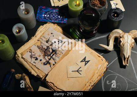 Zauberattribute der Hexe mit Kristallkugel des Wahrsagers und Buch auf dunklem Tisch Stockfoto