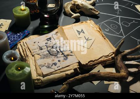 Zauberattribute der Hexe mit Buch und Kerzen auf dunklem Tisch Stockfoto