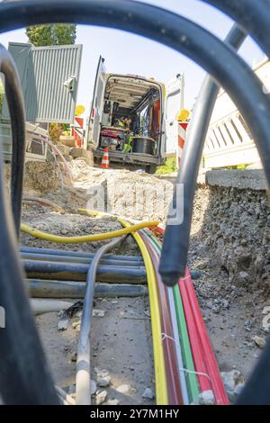 Eine Baustelle mit Glasfaserkabeln, technischen Geräten und einem geparkten Lkw, ein Arbeiter ist im Hintergrund beschäftigt, Glasfaserkabel installiert, dediziert Stockfoto