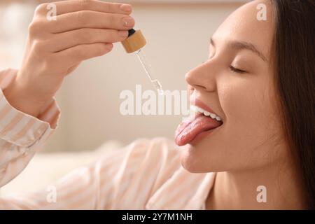 Junge Frau, die CBD-Öl im Schlafzimmer nimmt, Nahaufnahme Stockfoto