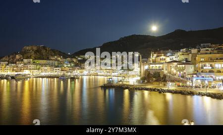 Beleuchtete Küstenstadt mit Vollmond und Wasser bei Nacht, aufsteigendem Vollmond, Pigadia, Stadt und Hafen, Pigadia Bay, Hauptort, Karpathos, Dodekanese Stockfoto