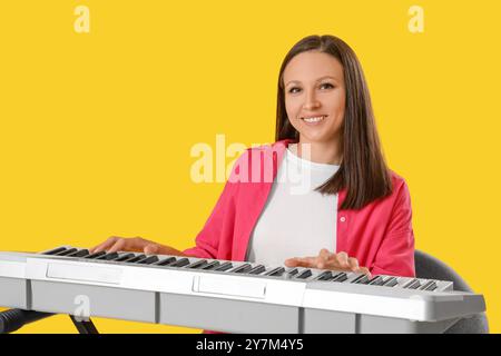 Junge Frau, die Synthesizer auf gelbem Hintergrund spielt Stockfoto