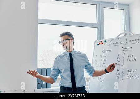 Selbstbewusster Englischlehrer, der im Klassenzimmer auf das Whiteboard zeigt Stockfoto