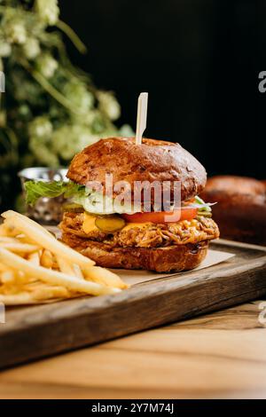 Saftiger Pulled Pork Burger mit Käse, Salat und Gurken serviert mit knusprigen Pommes frites an Bord Stockfoto