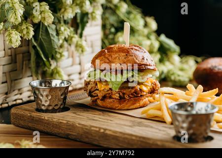 Saftiger Pulled Pork Burger mit Käse, Salat und Gurken serviert mit knusprigen Pommes frites an Bord Stockfoto