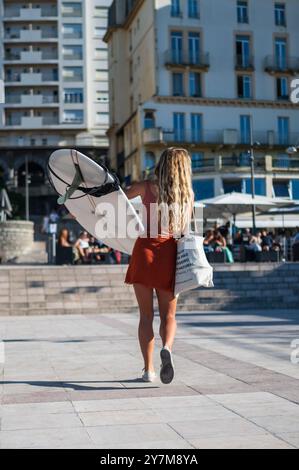 Eine junge Frau, die ihr Surfbrett am Strand Grande Plage in Biarritz trägt Stockfoto