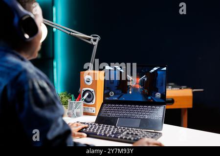 Fokussierter afroamerikanischer Spieler genießt kompetitives Gaming auf einem digitalen Notebook. Schnurlose Computer, Headset und digitale Grafiken sorgen für mehr Spannung bei Schwarzen beim Spielen eines Videospiels. Stockfoto