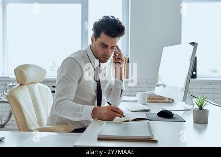 Selbstbewusster Mann in Hemd und Krawatte, der sich Notizen macht und telefoniert, während er im Büro sitzt Stockfoto