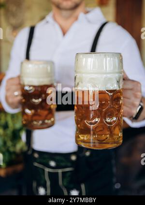 Mann in traditionellem bayerischem Outfit mit zwei Bierkrügen, perfekt für Oktoberfest, deutsche Feste Stockfoto