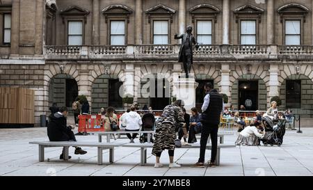 London, England, April 30 2023: Menschen sitzen draußen bei einer Bronzestatue an einem hellen Tag Stockfoto