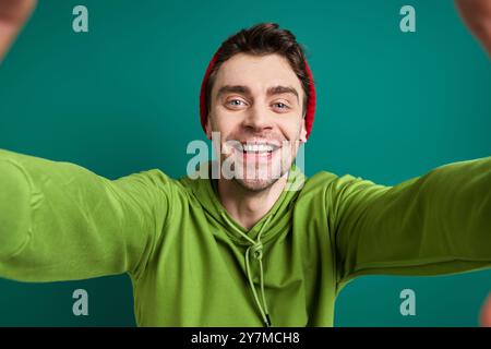 Glücklicher junger Mann, der durch einen Fingerrahmen schaut, während er vor grünem Hintergrund steht Stockfoto