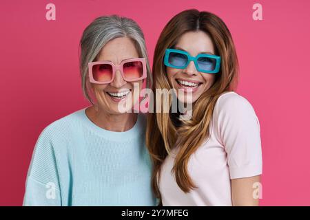 Glückliche Mutter und erwachsene Tochter in flippiger Brille vor rosa Hintergrund Stockfoto