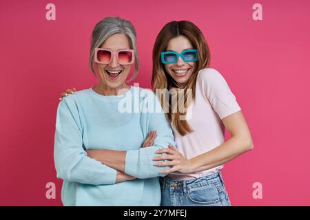 Verspielte Mutter und Erwachsene Tochter in funky Brille vor rosa Hintergrund Stockfoto