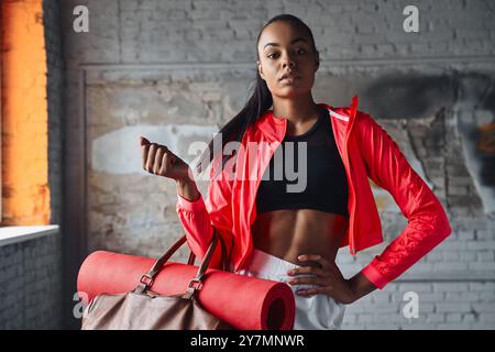 Schöne junge Afrikanerin in Sportbekleidung, die Tasche mit Bewegung trägt Stockfoto