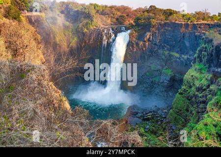 Ein atemberaubender Blick auf einen mächtigen Wasserfall, der in einen ruhigen Pool eintaucht, umgeben von üppigem Grün und zerklüfteten Klippen an einem hellen, sonnigen Tag, der an Stockfoto